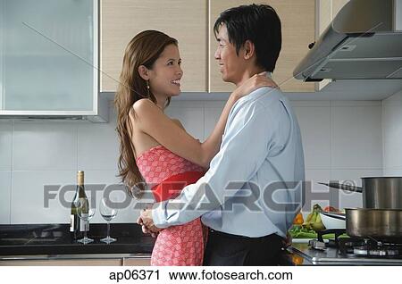 Stock Image - Couple embracing in kitchen. Fotosearch