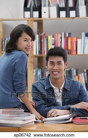 Stock Image - Couple in library, looking at camera. Fotosearch