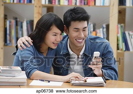 Couple in library, looking at mobile phone View Large Photo Image Stock Photo - Couple in library, looking at mobile phone. Fotosearch