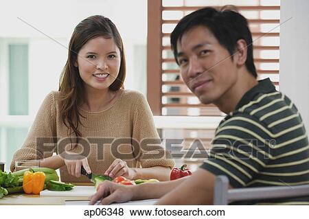 Couple looking at camera, woman chopping vegetables View Large Photo Image Stock Photo - Couple looking at camera, woman chopping vegetables. Fotosearch