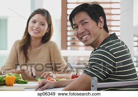 Couple looking at camera, woman chopping vegetables, focus on the man in foreground View Large Photo Image Stock Photo - Couple looking at camera, woman chopping vegetables, focus on the man in foreground. Fotosearch