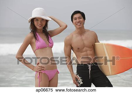 Stock Photography - Couple on beach, man carrying surfboard. Fotosearch