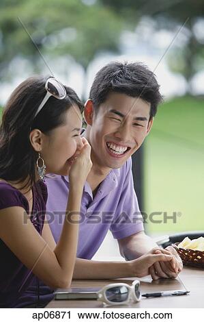 Couple sitting at cafe, young woman with hand over mouth, smiling View Large Photo Image Stock Image - Couple sitting at cafe, young woman with hand over mouth, smiling. Fotosearch