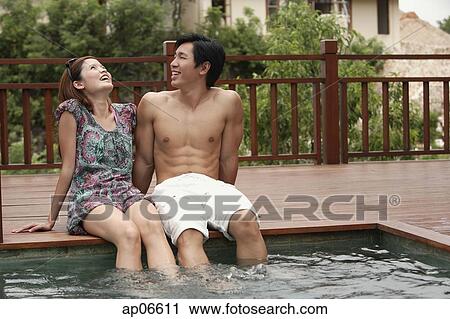 Couple sitting at the edge of swimming pool View Large Photo Image Stock Image - Couple sitting at the edge of swimming pool. Fotosearch