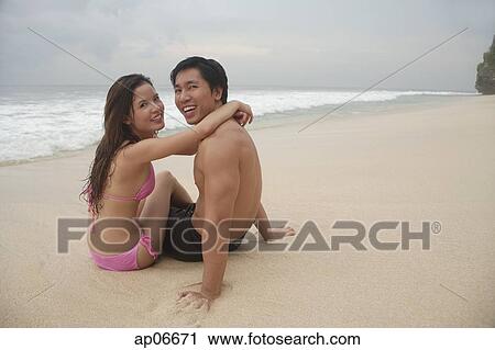 Couple sitting on beach, embracing, looking at camera View Large Photo Image Stock Image - Couple sitting on beach, embracing, looking at camera. Fotosearch