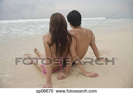 Stock Image - Couple sitting on beach, looking out to sea. Fotosearch