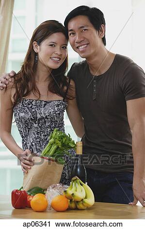 Stock Image - Couple smiling at camera, fresh fruits and vegetables on table in front of them. Fotosearch