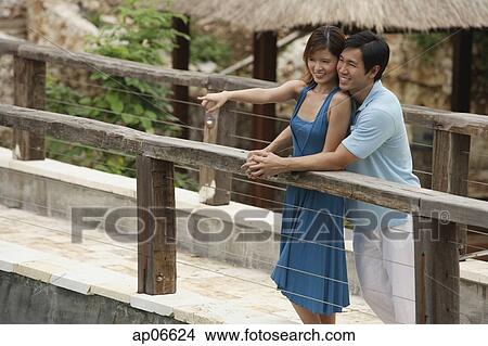 Couple standing side by side on bridge, woman pointing in the distance View Large Photo Image Picture - Couple standing side by side on bridge, woman pointing in the distance. Fotosearch