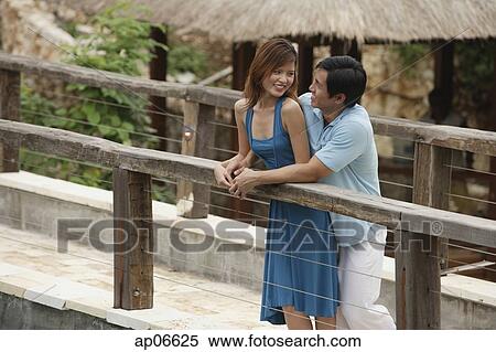 Stock Photography - Couple standing side by side on bridge, looking at each other. Fotosearch
