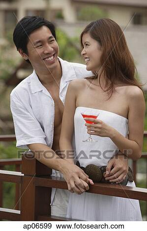 Stock Photo - Couple standing side by side on balcony, smiling at each other. Fotosearch
