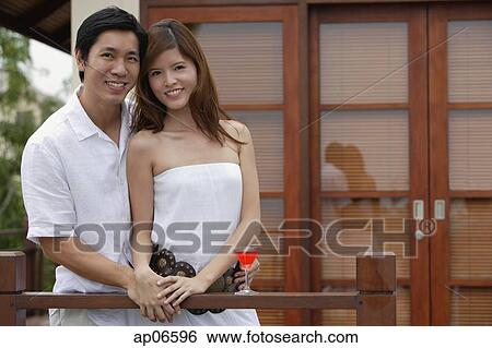 Stock Photograph - Couple standing side by side on balcony, smiling at camera. Fotosearch