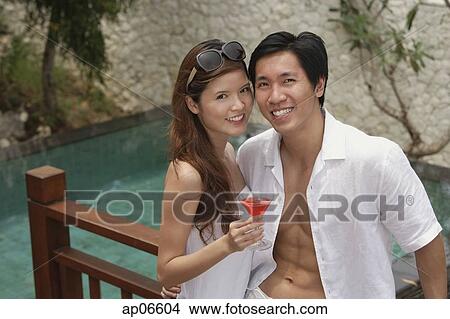 Couple standing side by side, smiling at camera, swimming pool behind them View Large Photo Image Picture - Couple standing side by side, smiling at camera, swimming pool behind them. Fotosearch