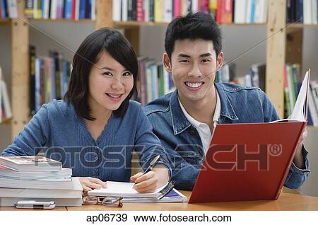 Stock Photo - Couple studying in library, smiling at camera. Fotosearch