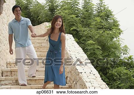 Stock Image - Couple walking down stairs, woman pulling man behind her. Fotosearch