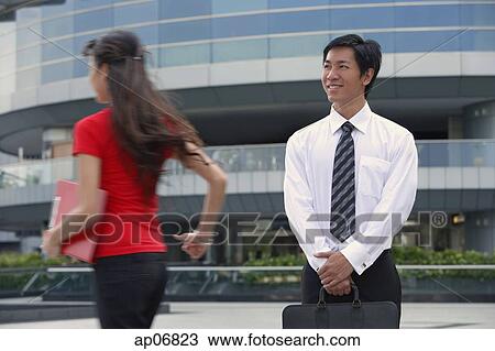 Stock Image - Male executive smiling at woman walking by. Fotosearch