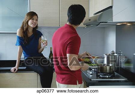 Man cooking in kitchen, looking at woman sitting on kitchen counter View Large Photo Image Stock Photo - Man cooking in kitchen, looking at woman sitting on kitchen counter. Fotosearch