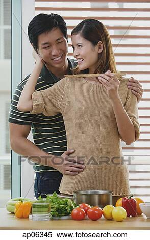 Man embracing woman from behind, woman feeding man View Large Photo Image Stock Photography - Man embracing woman from behind, woman feeding man. Fotosearch
