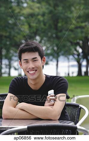 Man sitting at outdoor cafe, arms crossed, smiling View Large Photo Image Stock Photograph - Man sitting at outdoor cafe, arms crossed, smiling. Fotosearch