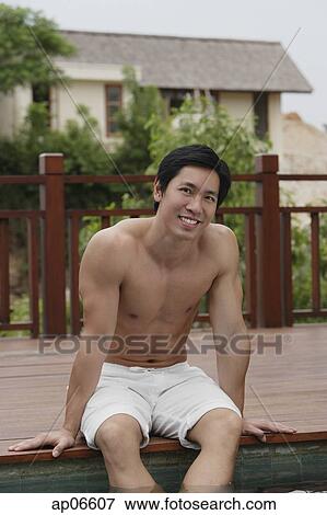Stock Photo - Man sitting at the edge of swimming pool, smiling at camera. Fotosearch