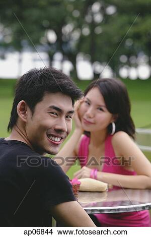 Picture - Man turning to smile at camera, woman in the background. Fotosearch
