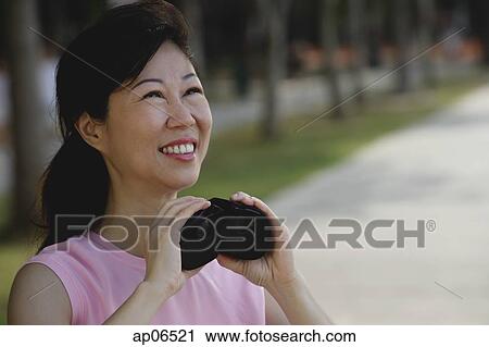 Stock Image - Mature woman holding binoculars, looking away. Fotosearch