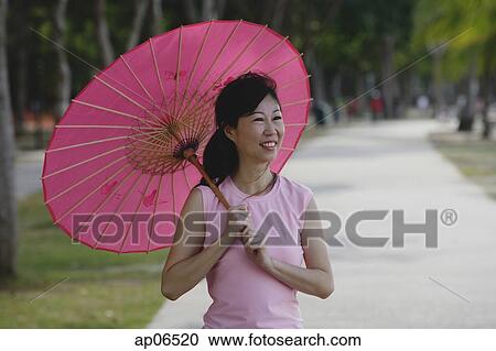 Stock Image - Mature woman using pink umbrella. Fotosearch