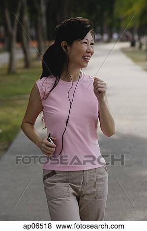 Mature woman walking in park, listening to MP3 player, smiling View Large Photo Image Stock Photo - Mature woman walking in park, listening to MP3 player, smiling. Fotosearch