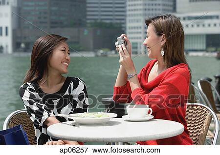 Two women at outdoor cafe, using a camera View Large Photo Image Stock Photo - Two women at outdoor cafe, using a camera. Fotosearch