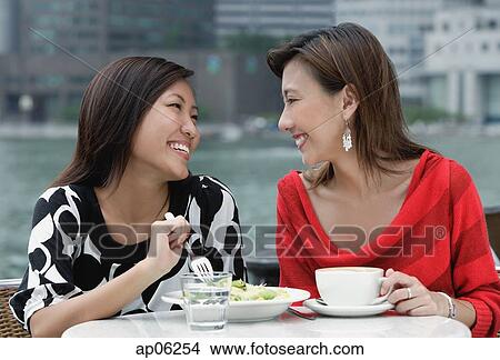 Picture - Two women at sidewalk cafe having lunch, smiling at each other. Fotosearch