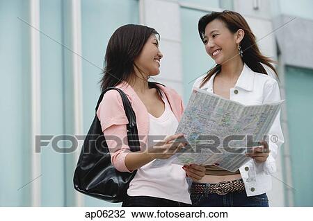 Stock Image - Two women with map, smiling at each other. Fotosearch
