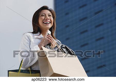 Woman carrying shopping bags, holding mobile phone, smiling View Large Photo Image Stock Image - Woman carrying shopping bags, holding mobile phone, smiling. Fotosearch