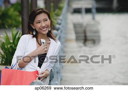 Woman carrying shopping bags, holding mobile phone, smiling View Large Photo Image Stock Photo - Woman carrying shopping bags, holding mobile phone, smiling. Fotosearch