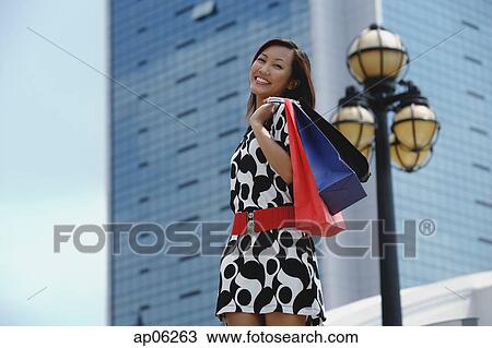Stock Image - Woman carrying shopping bags, smiling at camera. Fotosearch