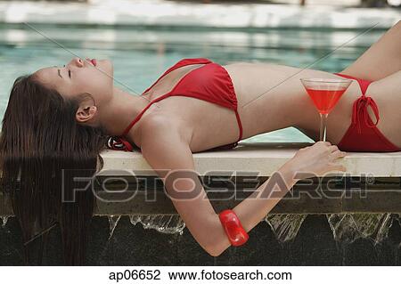 Woman in red bikini lying at the edge of swimming pool, holding cocktail, eyes closed View Large Photo Image Stock Image - Woman in red bikini lying at the edge of swimming pool, holding cocktail, eyes closed. Fotosearch