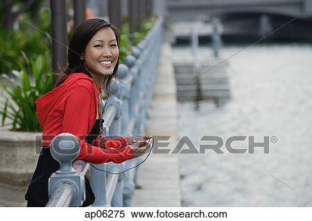 Woman leaning on railing, listening to MP3 player, smiling at camera View Large Photo Image Stock Photography - Woman leaning on railing, listening to MP3 player, smiling at camera. Fotosearch