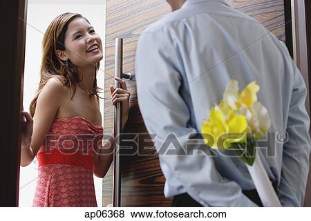 Stock Photo - Woman opening door, man with flowers behind his back. Fotosearch