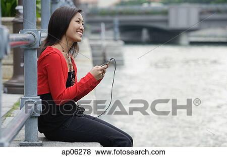 Woman sitting by river, listening to MP3 player View Large Photo Image Stock Photo - Woman sitting by river, listening to MP3 player. Fotosearch