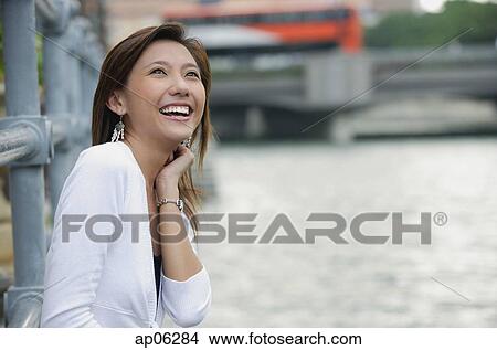 Woman sitting by river, smiling, looking up View Large Photo Image Picture - Woman sitting by river, smiling, looking up. Fotosearch