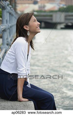 Woman sitting by river, smiling, looking up View Large Photo Image Stock Image - Woman sitting by river, smiling, looking up. Fotosearch