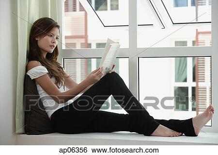 Stock Photograph - Woman sitting by window reading a book. Fotosearch