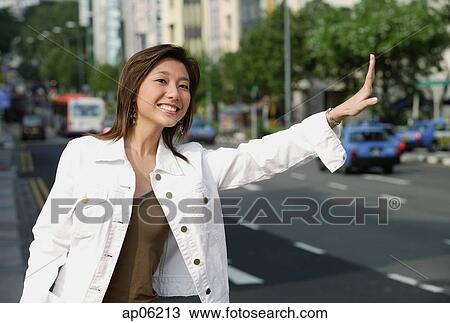 Stock Image - Woman standing by road, waving for taxi. Fotosearch