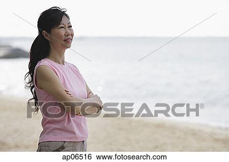 Woman standing on beach, arms crossed, looking away View Large Photo Image Stock Photograph - Woman standing on beach, arms crossed, looking away. Fotosearch