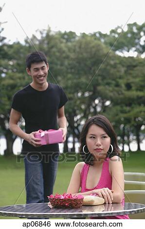 Woman waiting at outdoor cafe, man in background, holding a present View Large Photo Image Stock Photograph - Woman waiting at outdoor cafe, man in background, holding a present. Fotosearch