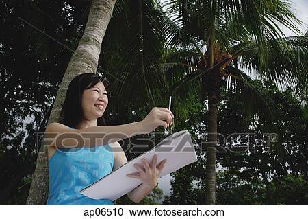 Woman with sketchbook standing under a coconut tree View Large Photo Image Stock Image - Woman with sketchbook standing under a coconut tree. Fotosearch