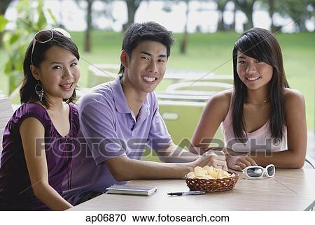Stock Image - Young adults sitting at outdoor cafe, smiling at camera. Fotosearch