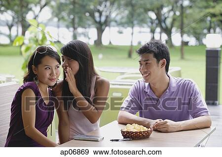 Young adults sitting at outdoor cafe, women whispering in each others ears, man looking on View Large Photo Image Stock Photo - Young adults sitting at outdoor cafe, women whispering in each others ears, man looking on. Fotosearch
