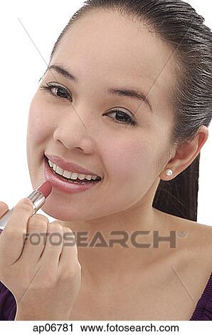 Stock Image - Young woman applying lipstick, smiling. Fotosearch