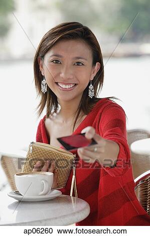 Stock Image - Young woman at cafe, holding credit card towards camera. Fotosearch