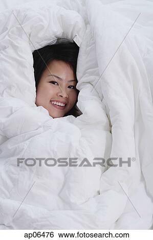 Young woman covered by blanket, smiling at camera View Large Photo Image Stock Photograph - Young woman covered by blanket, smiling at camera. Fotosearch