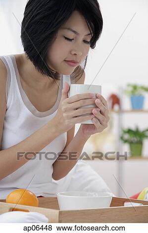 Young woman having breakfast, holding coffee mug View Large Photo Image Stock Photo - Young woman having breakfast, holding coffee mug. Fotosearch
